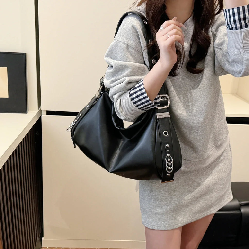Porté à l'épaule sur une robe sweat grise, le hobo noir clouté descend jusqu'à la hanche