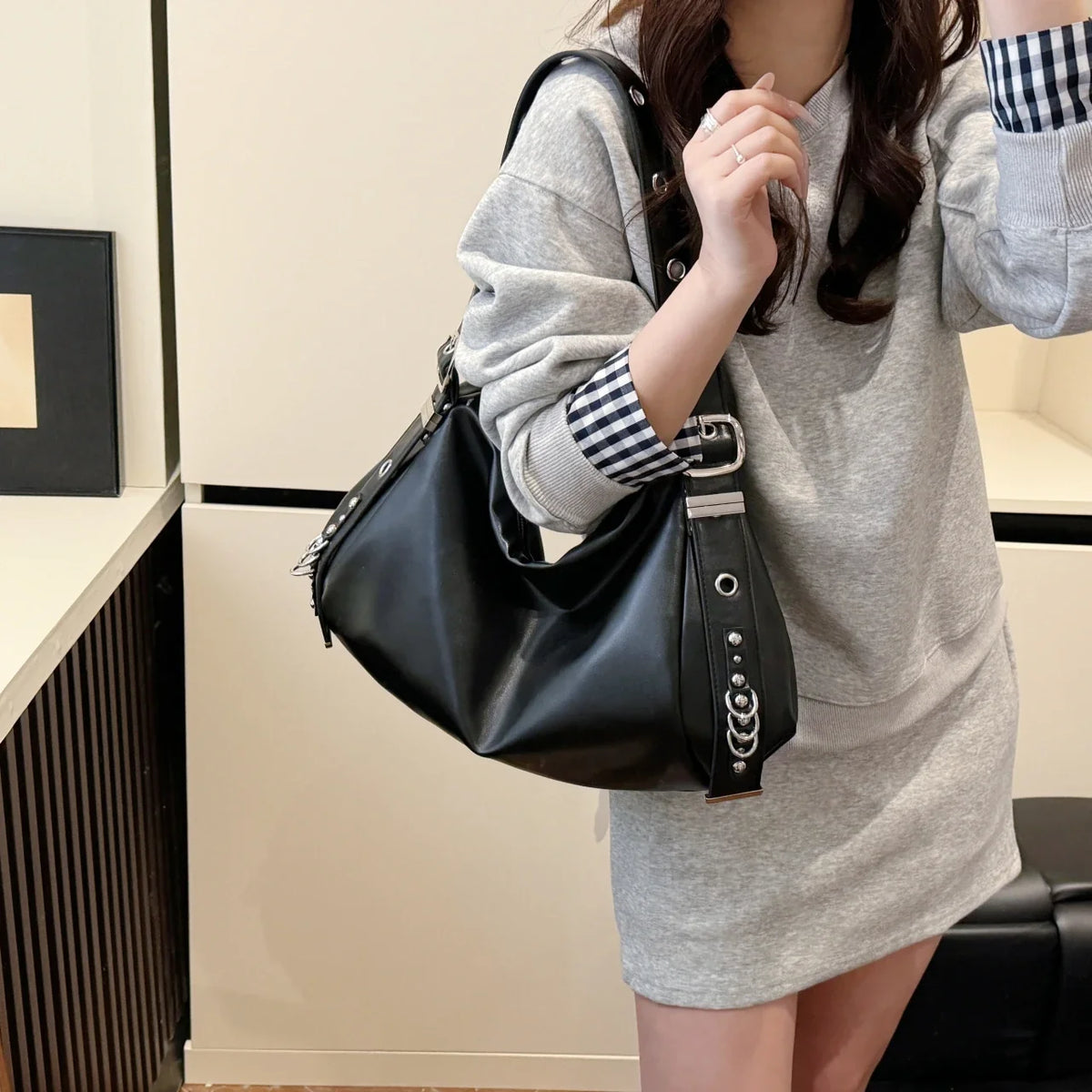 Porté à l'épaule sur une robe sweat grise, le hobo noir clouté descend jusqu'à la hanche