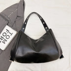 Posé sur un plaid blanc à côté d'une veste grise, le sac noir clouté montre sa base souple