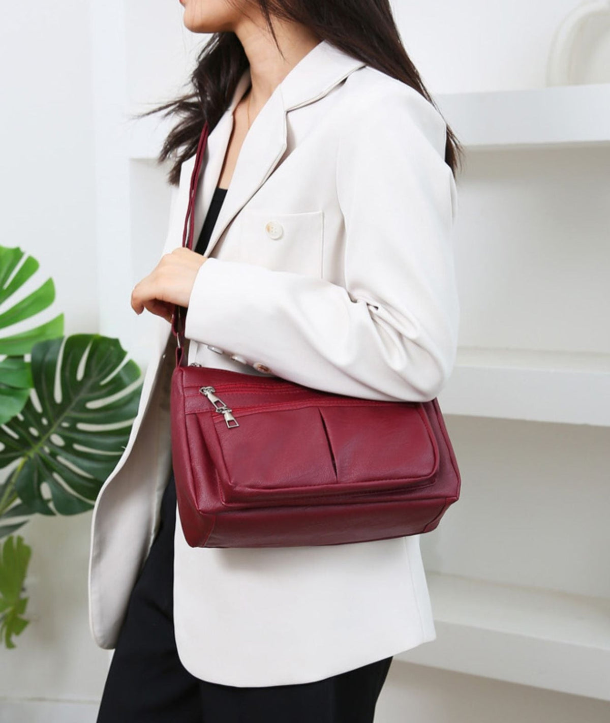 Sangle en travers d'un blazer blanc, le sac bordeaux se tient plaqué contre la hanche