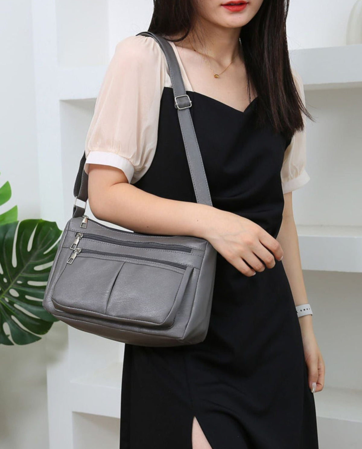 En bandoulière sur une robe noire, le sac gris repose à hauteur de hanche, sangle sur l'épaule