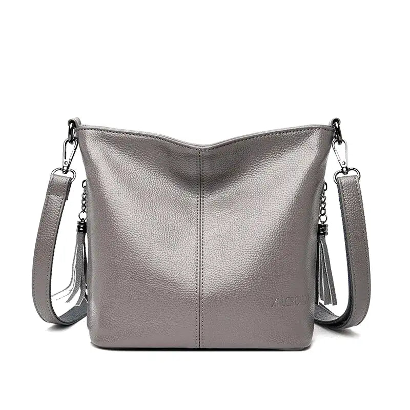 Gris perle satiné, ce petit sac seau se présente de face, sangle réglable et pampille latérale