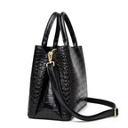 Profil du sac croco noir, soufflet latéral marqué et mousqueton doré de la bandoulière