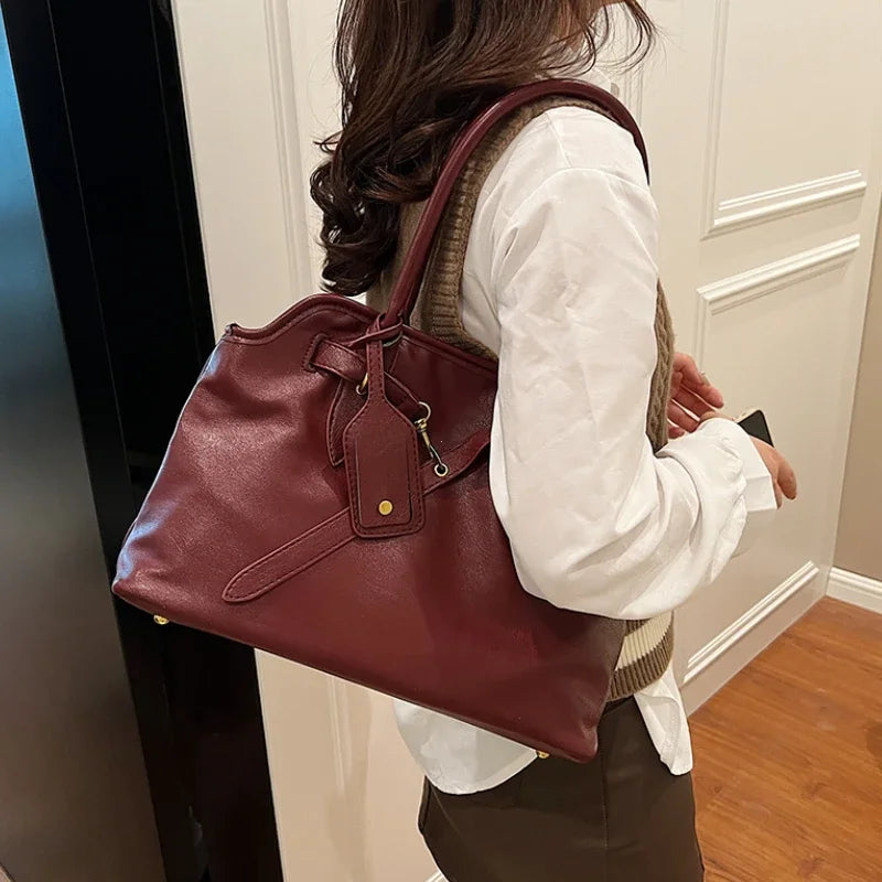 Modèle bordeaux porté à l'épaule sur une chemise blanche, il descend jusqu'à la hanche
