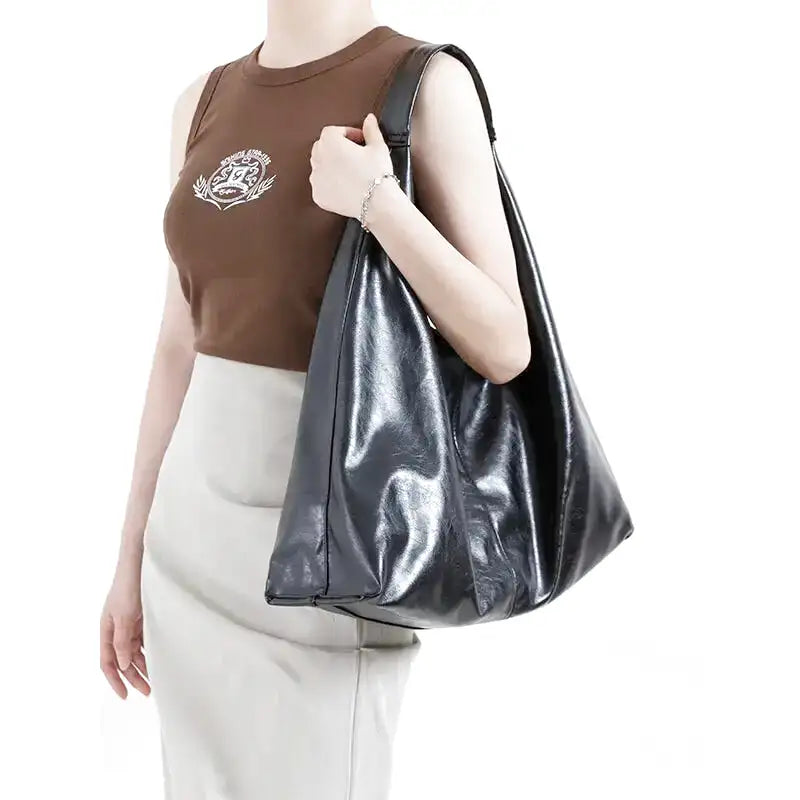 Reflets du cuir végan ciré noir, sac tenu à l'épaule sur un débardeur brun et une jupe claire