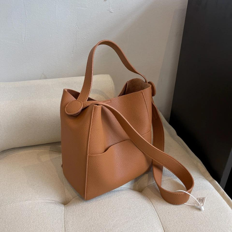 Modèle caramel posé sur un fauteuil bouclette écru, bandoulière déroulée sur l'assise
