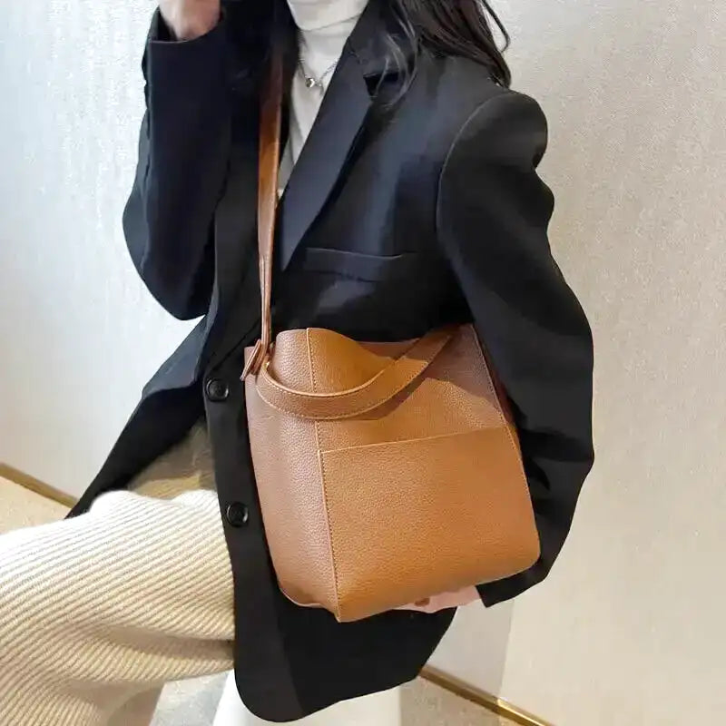 Porté en croisé sur un blazer noir, le sac seau cognac repose sur la hanche, anse souple