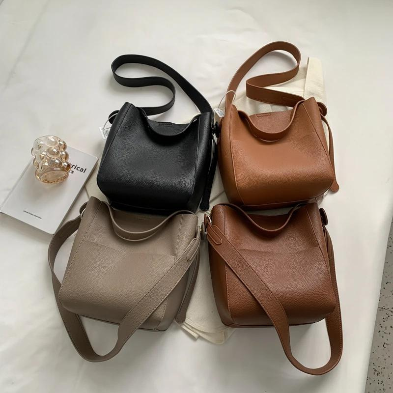 Quatre coloris du sac seau réunis à plat : noir, cognac, taupe et brun, sangles étalées