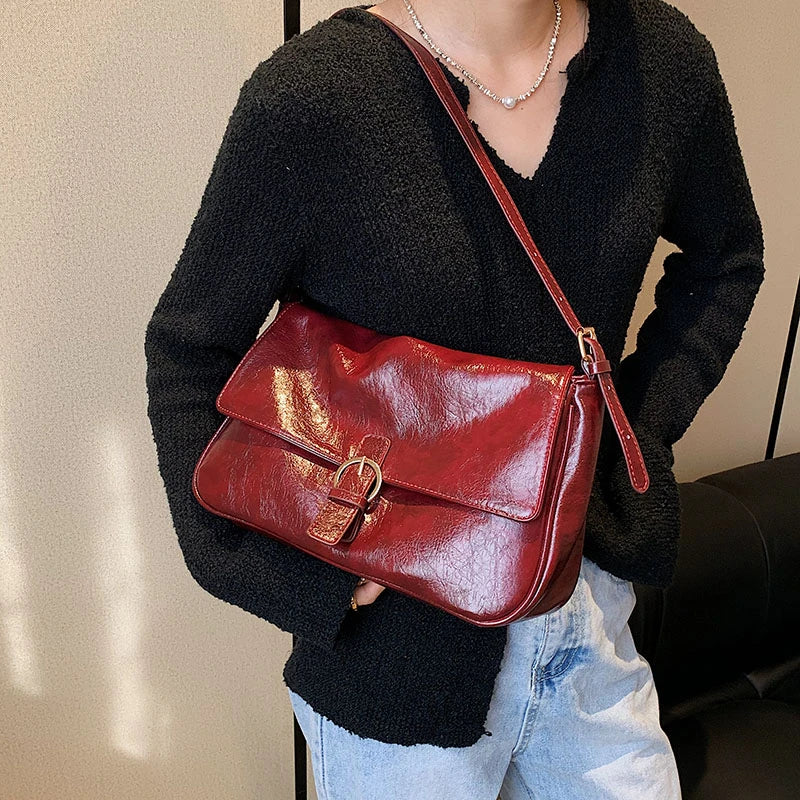 Croisée sur un pull noir, la besace rouge bordeaux repose sur la hanche, boucle ronde en évidence