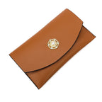 Pochette longue en cuir végan cognac fermée par un bouton fantaisie serti, posée à plat