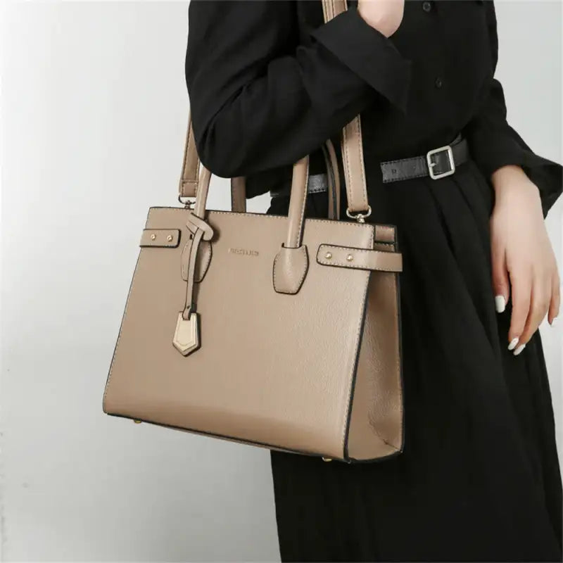Au creux du bras sur une tenue noire, le sac trapèze taupe garde sa forme bien droite