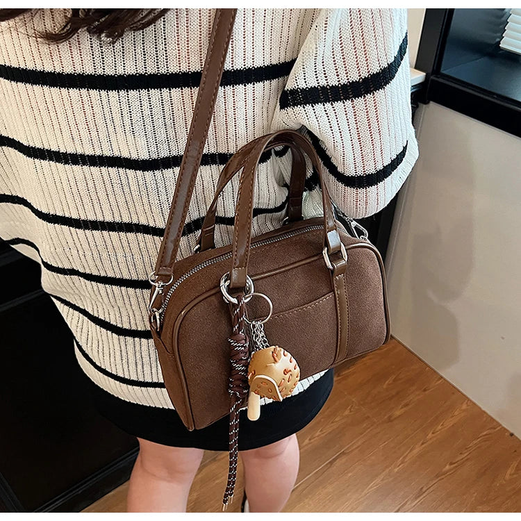 En bandoulière sur un pull rayé écru et noir, le sac bowling marron repose contre la hanche