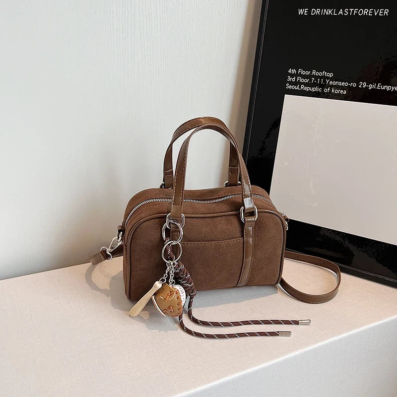 Posé sur un meuble clair devant un cadre noir, le sac bowling marron laisse pendre sa breloque