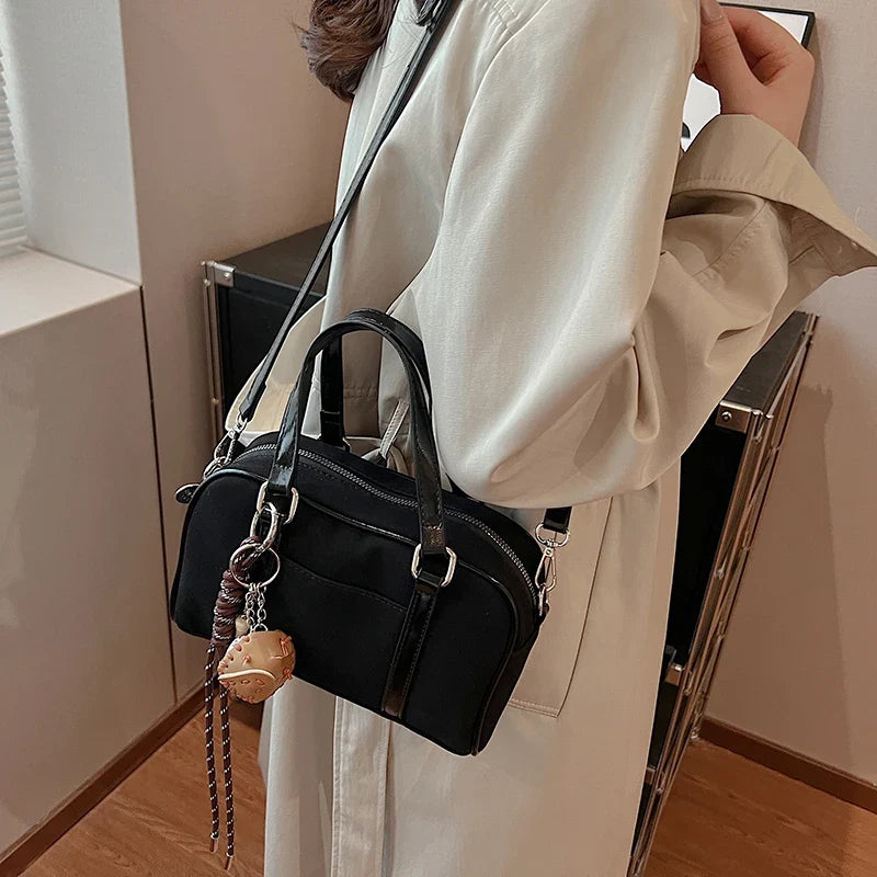 Suspendu à l'épaule par-dessus un trench beige, le sac bowling noir balance sa breloque tressée