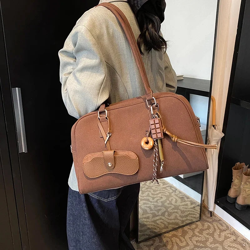 Sur l'épaule d'une passante en veste écrue, le sac bowling caramel se porte par ses anses courtes