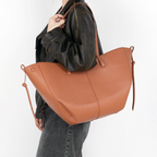 Épaule chargée du cabas cognac par-dessus une veste noire, silhouette en jean gris foncé
