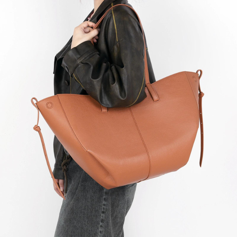 Épaule chargée du cabas cognac par-dessus une veste noire, silhouette en jean gris foncé