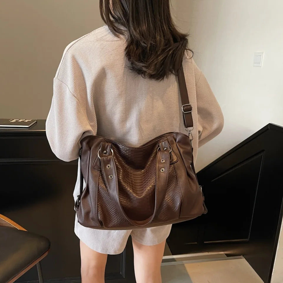 De dos, le cabas brun chocolat porté en croisé retombe sur un sweat écru et un short clair
