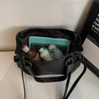 Intérieur du cabas noir ouvert, rempli d'une trousse, d'une boîte turquoise et de peluches