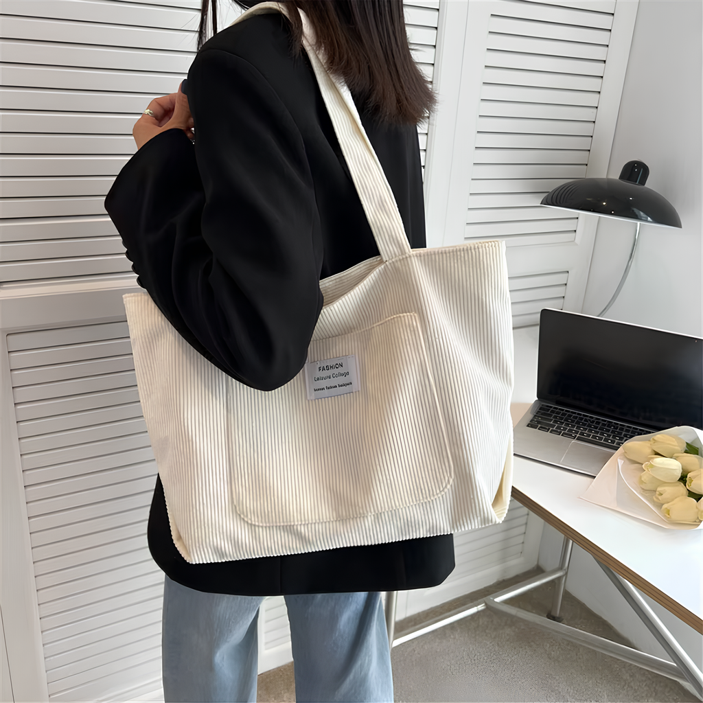 Velours côtelé crème porté à l'épaule sur une veste noire, devant un bureau et un ordinateur portable