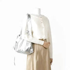 Hobo argenté à l'épaule sur une tenue crème et beige, volume souple retombant sous le bras