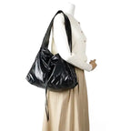 Mannequin en veste écrue portant le hobo noir sur l'épaule, la matière brillante forme des plis
