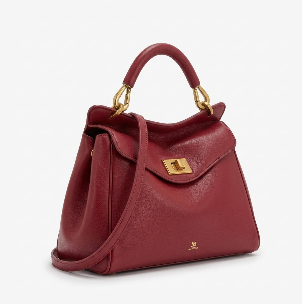 De trois quarts, le sac rouge bordeaux laisse voir ses soufflets souples et sa bandoulière
