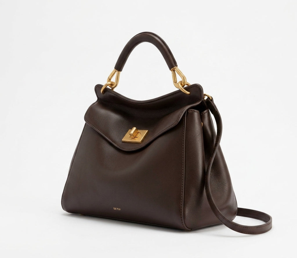 Profil trois quarts du sac brun chocolat, anse rigide arrondie et attaches dorées en crochet