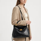 Croisé sur un blazer beige, le petit sac noir à fermoir doré repose à hauteur de hanche