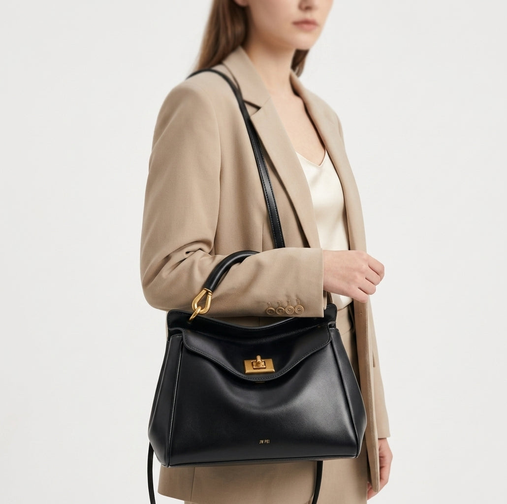 Croisé sur un blazer beige, le petit sac noir à fermoir doré repose à hauteur de hanche