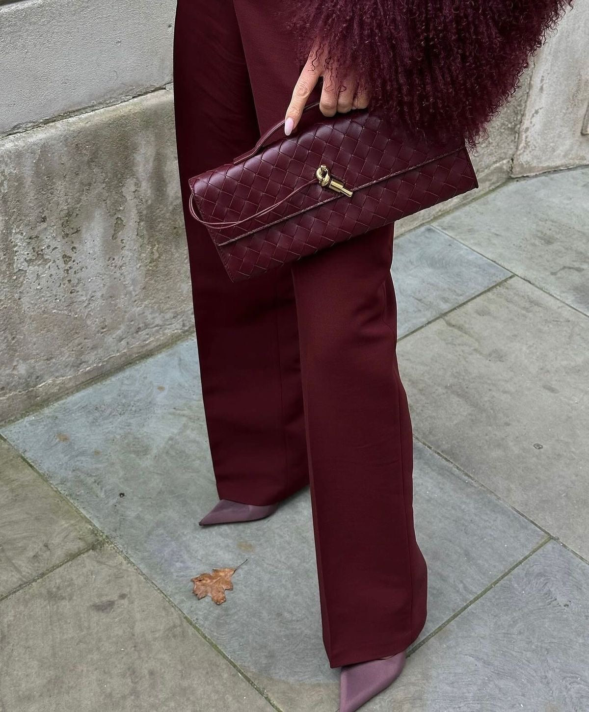 Silhouette en tailleur bordeaux tenant la pochette tressée assortie, fermoir doré bien au centre