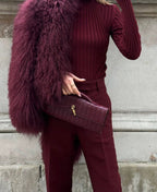 Tenue à la main devant une veste duveteuse prune, la pochette bordeaux tressée capte la lumière