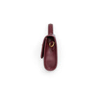 Tranche arrondie de la pochette bordeaux posée debout, anneau doré et soufflet latéral apparents