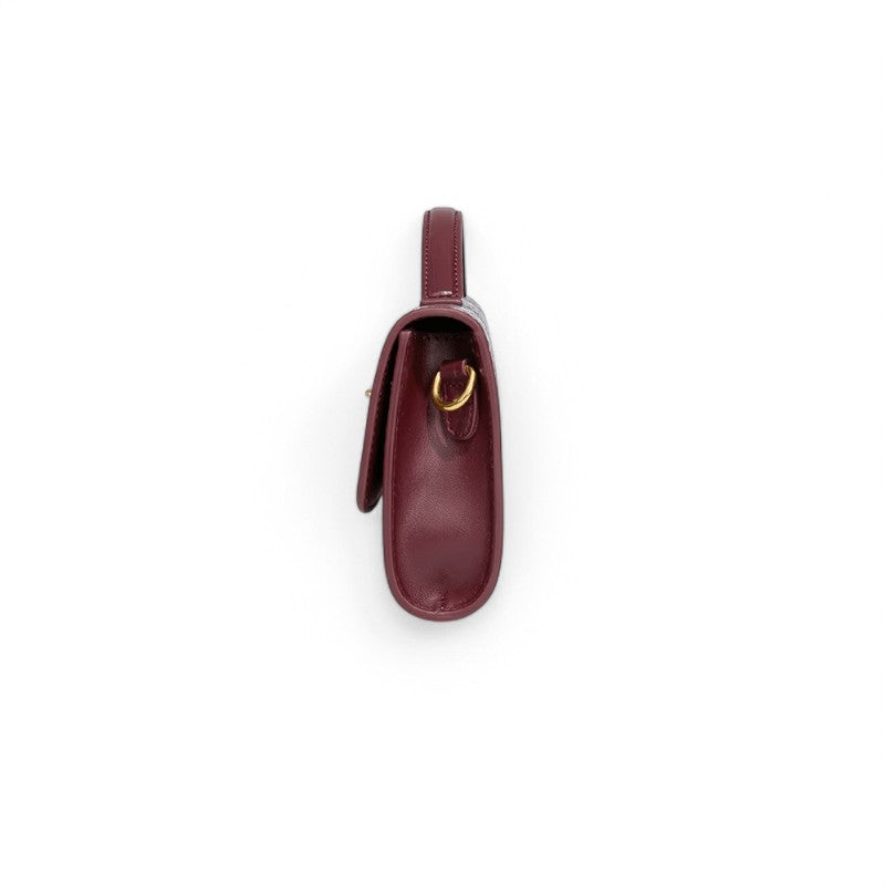 Tranche arrondie de la pochette bordeaux posée debout, anneau doré et soufflet latéral apparents
