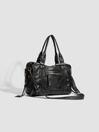 Longue bandoulière déployée au sol à droite du sac noir, mousquetons laiton et coulisses latérales