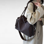 Épaule chargée du sac brun foncé, dont la bandoulière pend le long d'un manteau beige