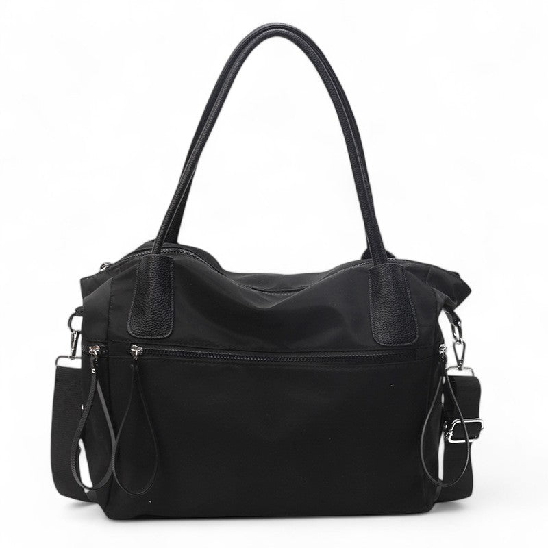 Toile noire et cuir végan assortis, le fourre-tout montre sa poche zippée avant et ses anses