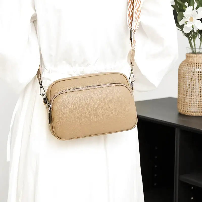 En travers du buste sur une robe blanche, la besace beige sable reste à hauteur de taille