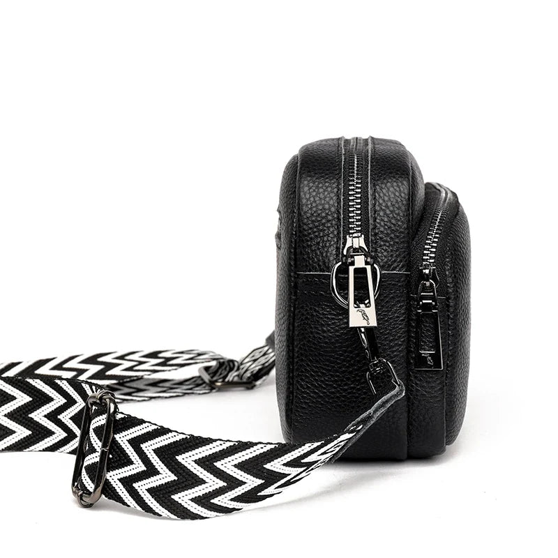 Profil du sac noir posé debout, les deux compartiments zippés et la sangle repliée au sol