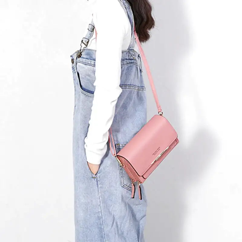 Croisée sur une salopette en jean, la pochette rose repose bas sur la hanche, sangle en diagonale