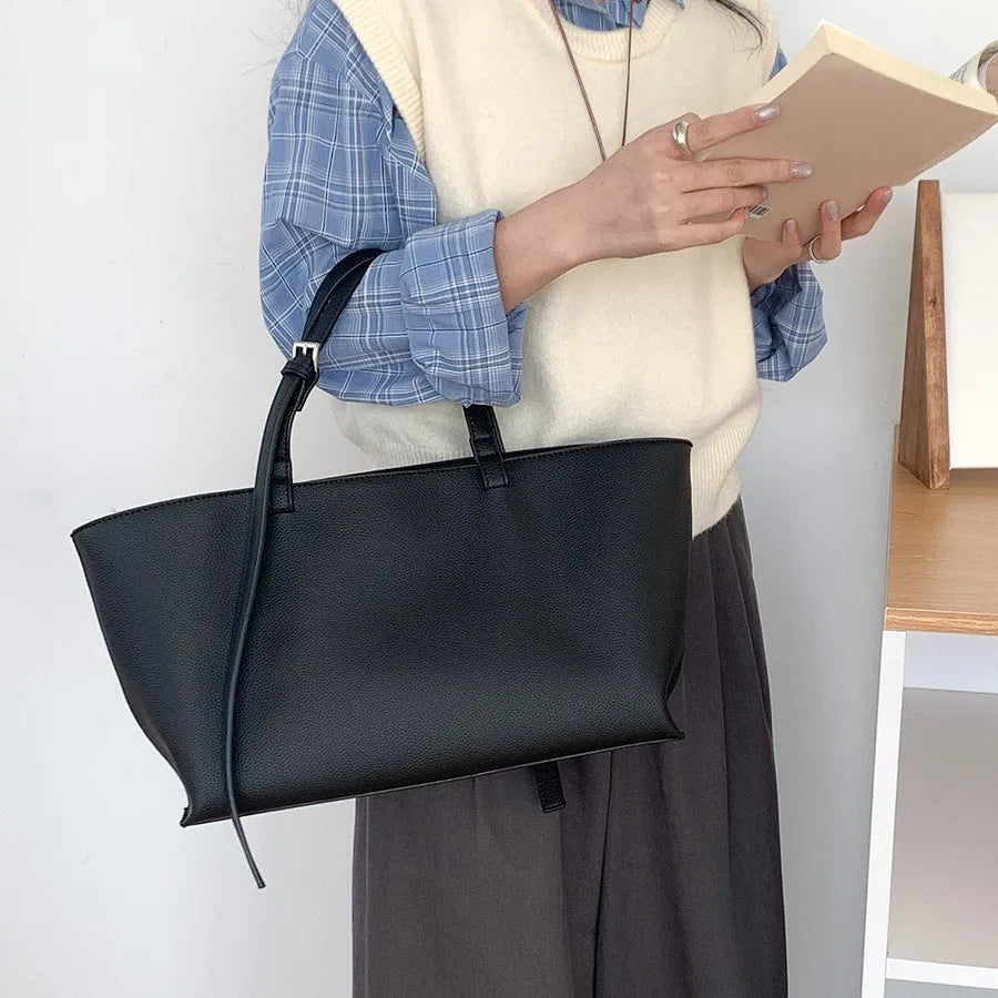 Debout un livre à la main, elle porte le fourre-tout noir à l'épaule sur un pantalon gris