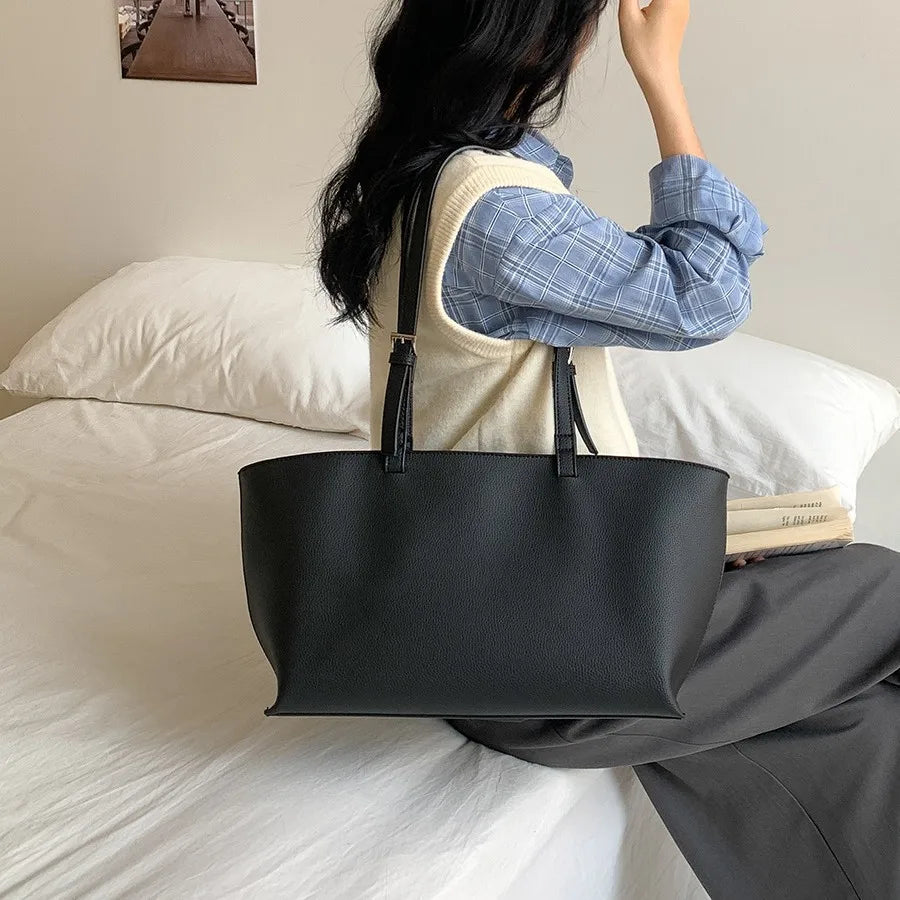 Assise sur un lit, une jeune femme porte le grand cabas noir à l'épaule, sac largement ouvert