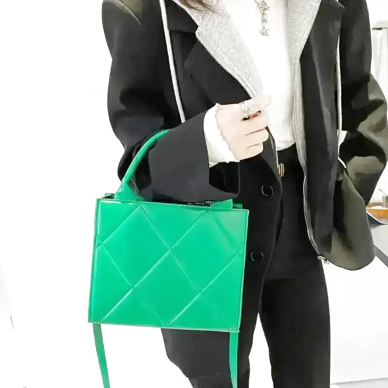 Anse rigide saisie à la main, le sac vert tranche sur un manteau noir et un pull blanc