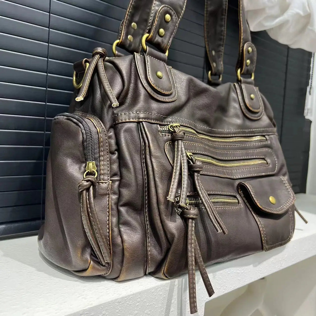 Gros plan du hobo bronze posé sur un rebord, grain froissé et tirants de zip en cuir végan
