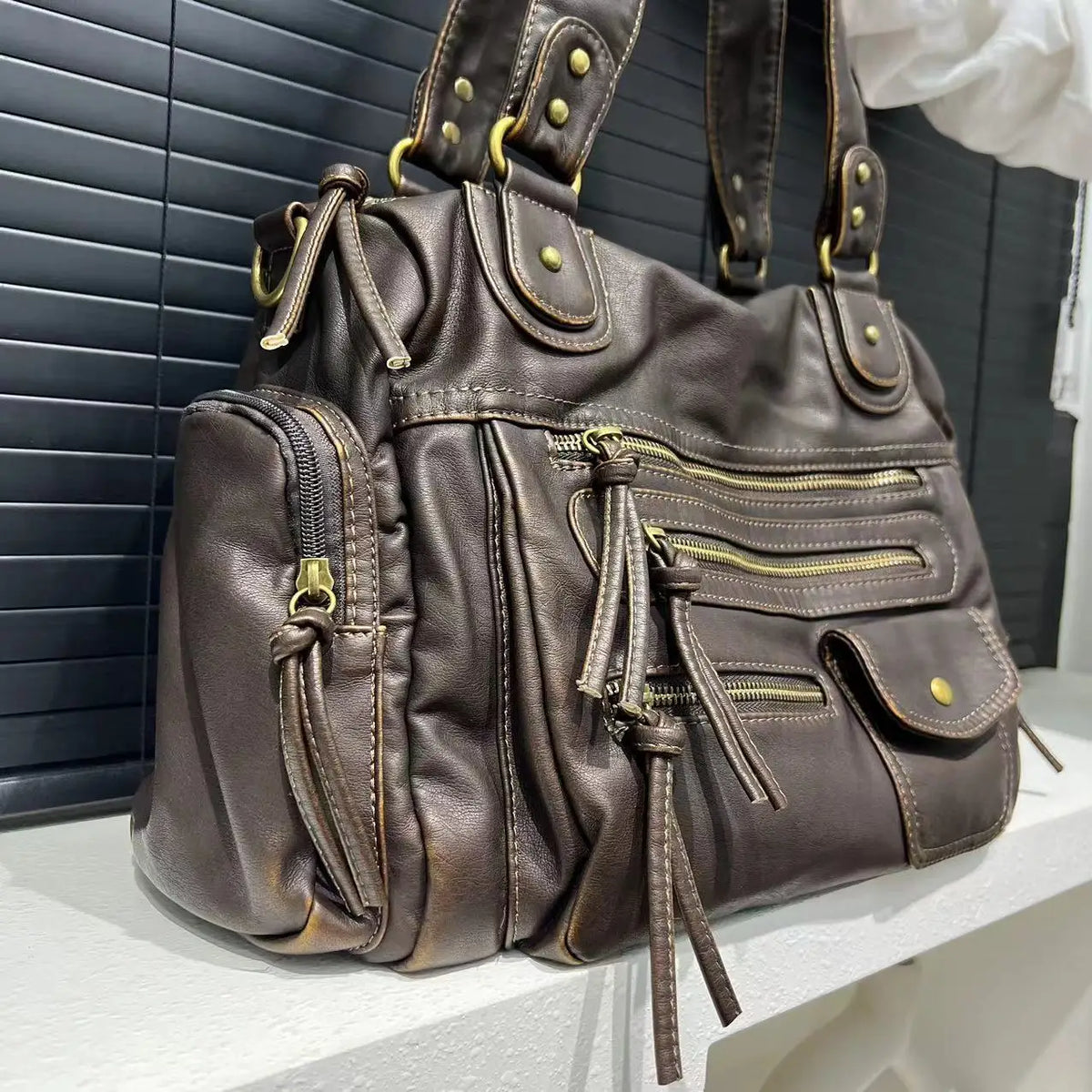 Gros plan du hobo bronze posé sur un rebord, grain froissé et tirants de zip en cuir végan