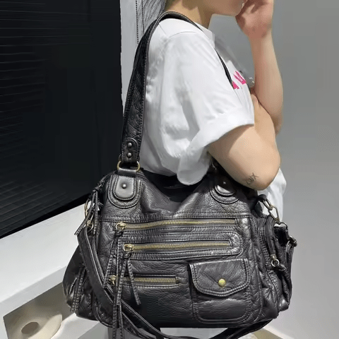 À l'épaule sur un tee-shirt blanc, le hobo noir montre ses zips obliques et sa poche à rabat
