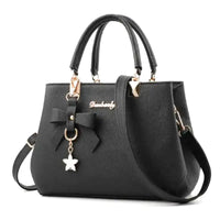 Sac à main noir en cuir végan à grain fin, vu de face, nœud décoratif et breloque étoile dorée