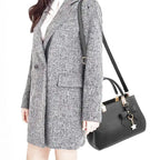 À l'épaule d'un modèle en manteau gris chiné, le sac noir tombe au niveau de la hanche