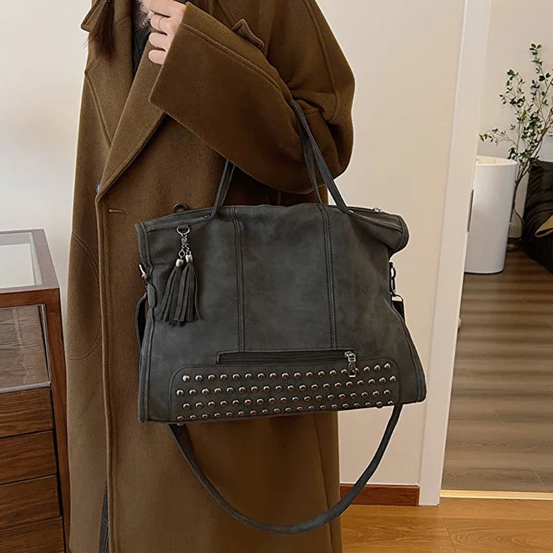 Anthracite et rangée de rivets, le cabas repose sur l'avant-bras devant un manteau camel