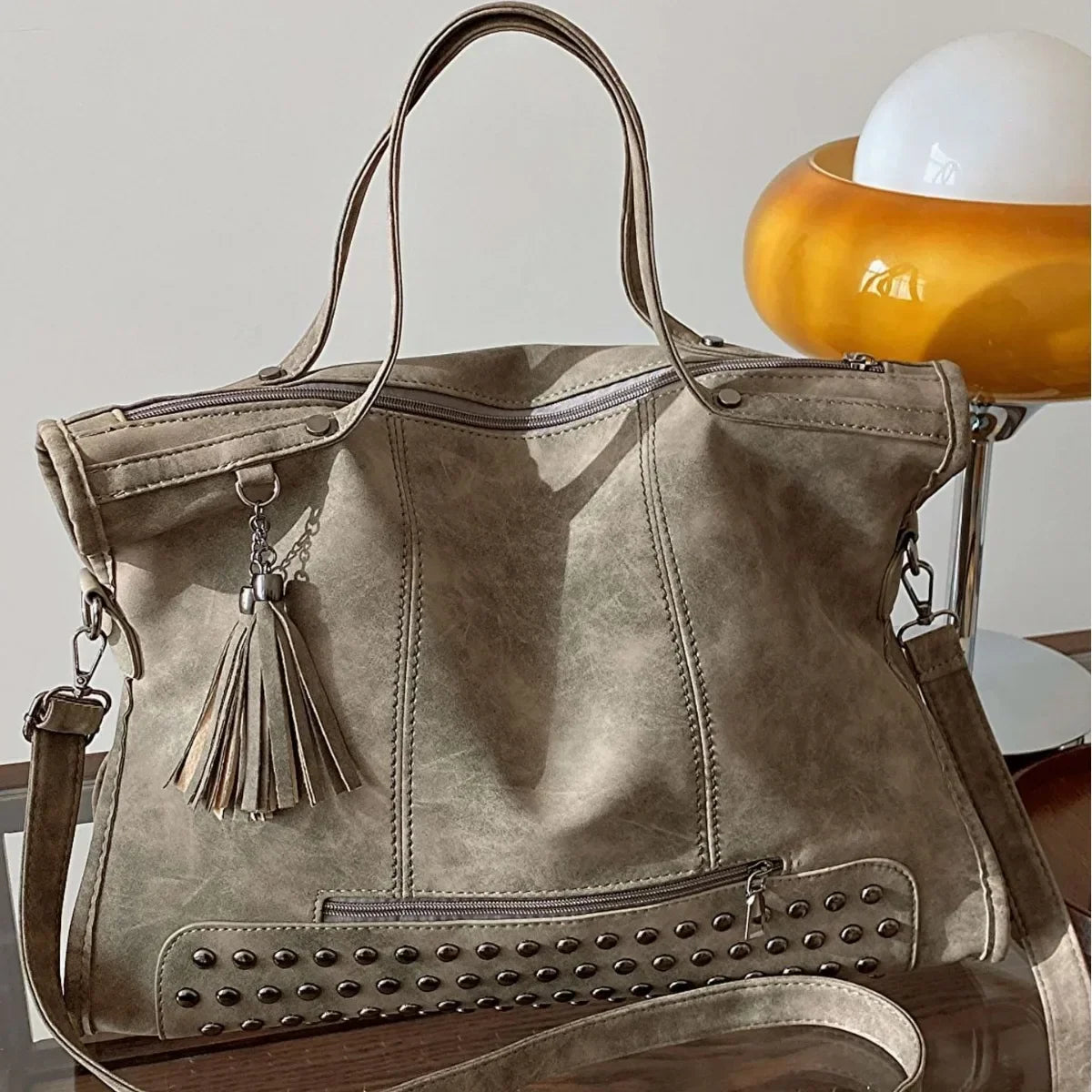 Effet nubuck taupe, ce cabas volumineux pose près d'une lampe, anses doubles et sangle longue